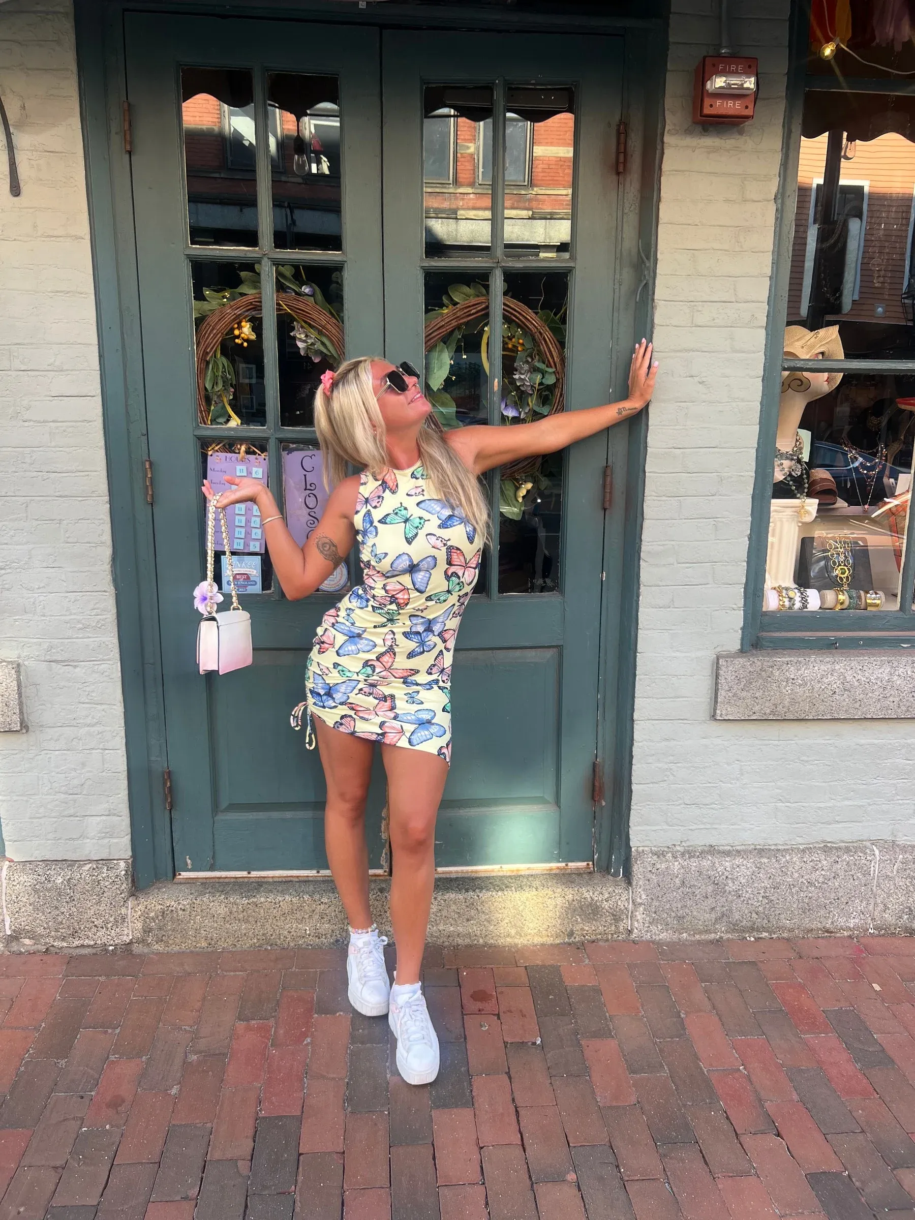 Gabriella posing in a butterfly-print dress beside a green-framed glass door