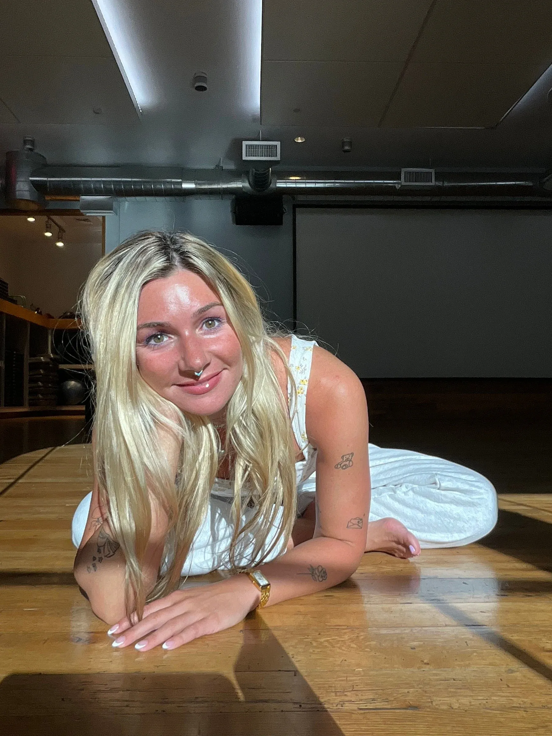 Gabriella lying on a sunlit wooden studio floor, smiling toward the camera
